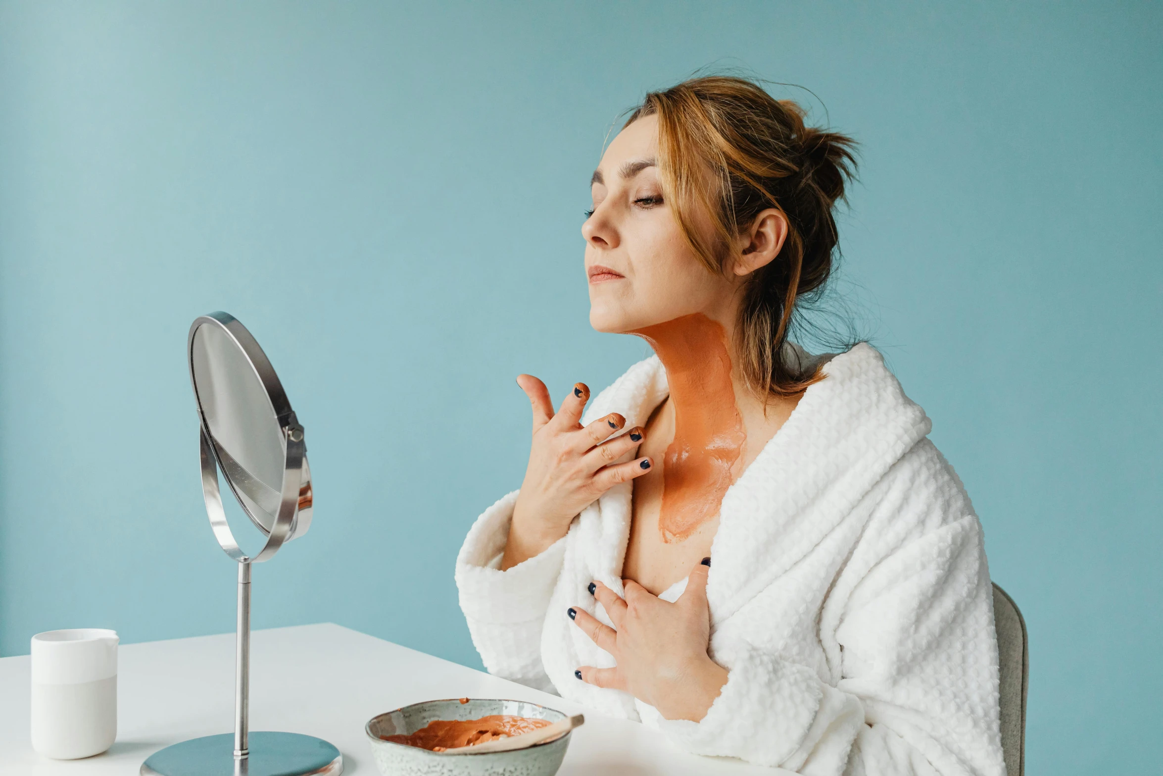 woman in white robe looking into mirror