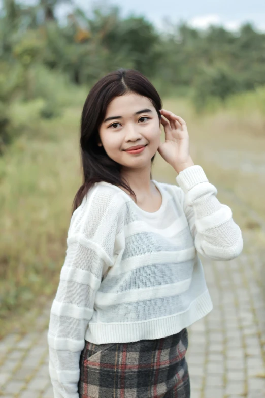 a beautiful young woman standing in a field with a white sweater on