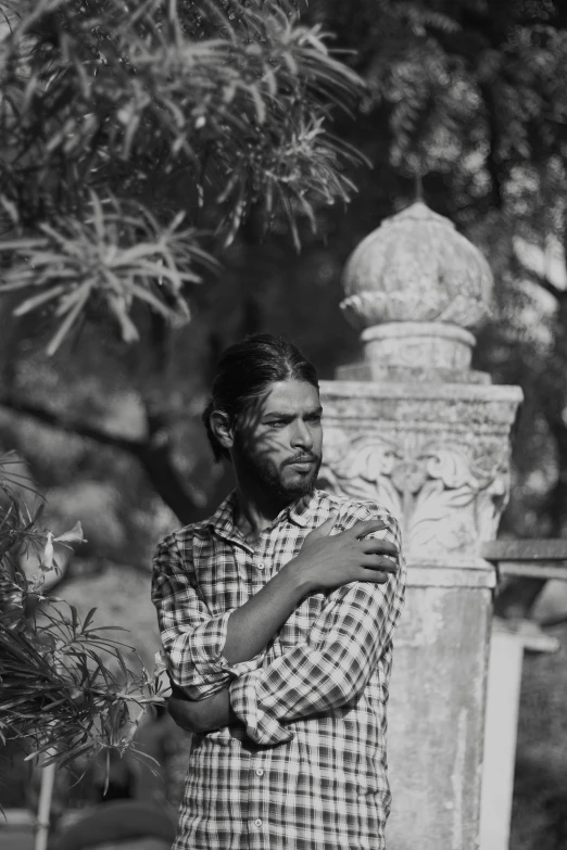 a man with a beard and plaid shirt standing by tree