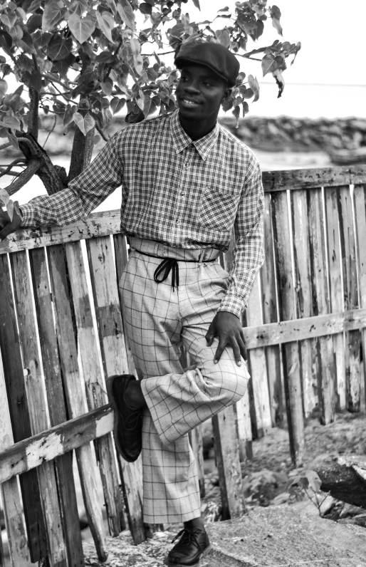 a black man leans against a fence while posing for a picture