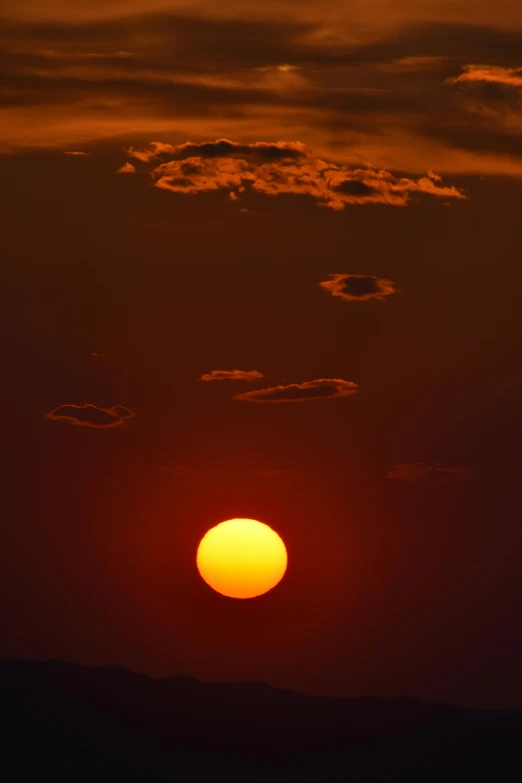 an orange sun in the horizon against some dark clouds