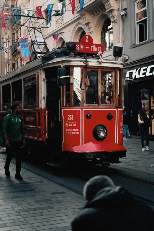 a red trolley car passing by people walking around