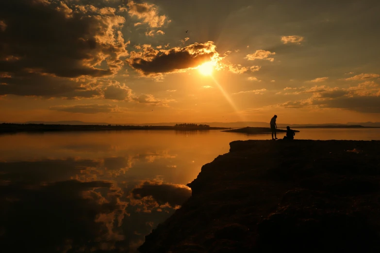 the two people are standing on the edge of a pier watching the sun go down