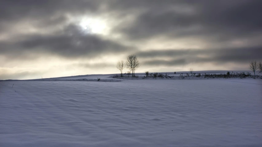 the sun shines through cloudy skies on a snowy slope