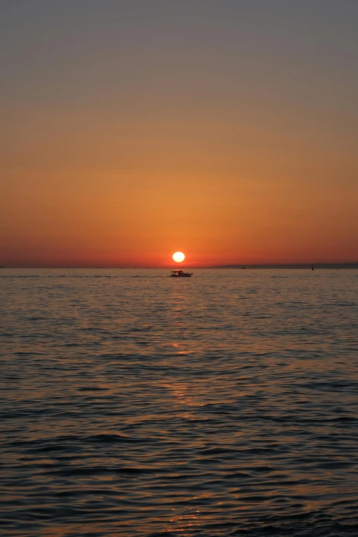 the sun sets over the water and small boat