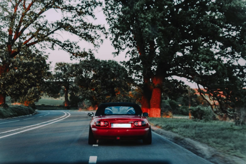 a red convertible driving down a road next to trees