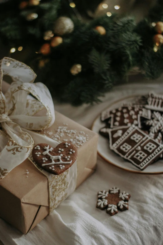 a present box tied with a white ribbon next to two decorated cookies on a table