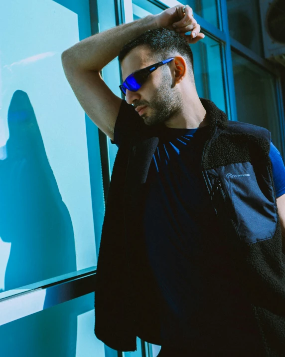 man in black and blue posing for the camera with his arm resting on his head