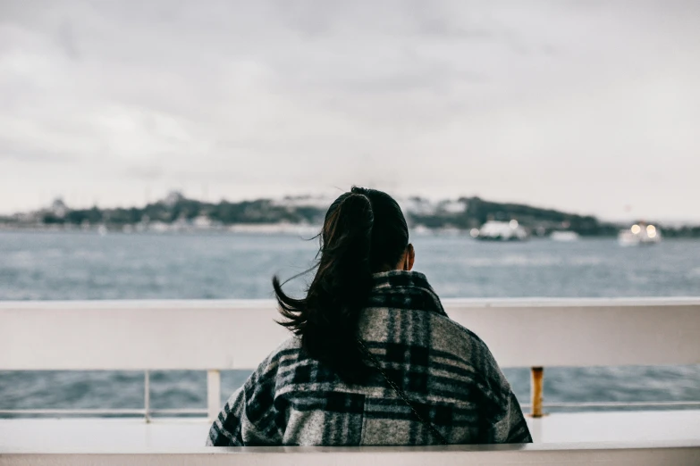 the woman sitting at a bench looks out over the ocean