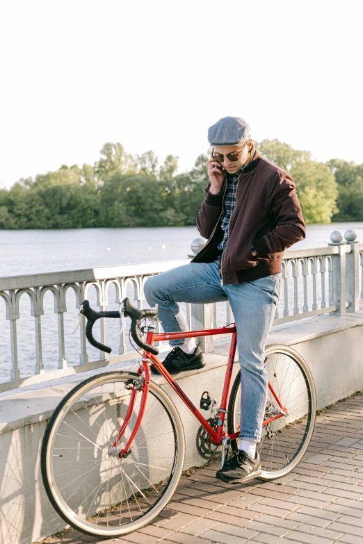 a young man on a red bike, sitting on a concrete bridge