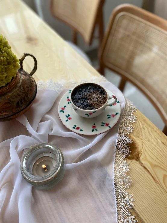 a cup of coffee next to an old tea kettle on a table