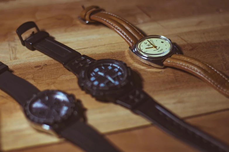 four different styles of wrist watches are sitting on a wooden surface