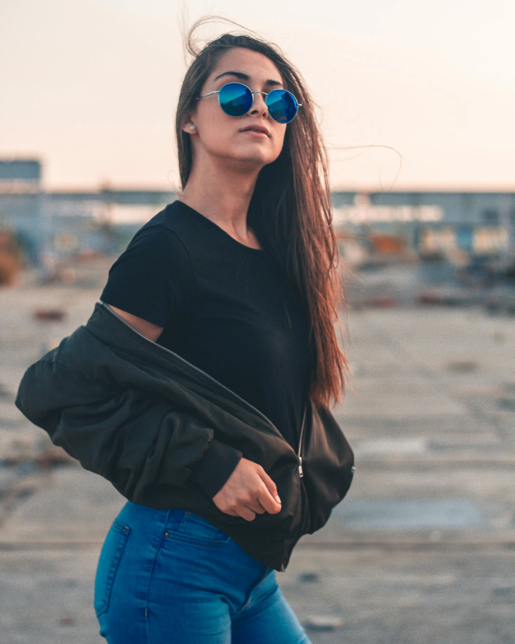 a girl with her hair blowing in the wind wearing blue jeans and black top