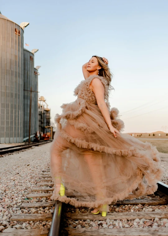 an attractive young woman in a dress is posing on train tracks