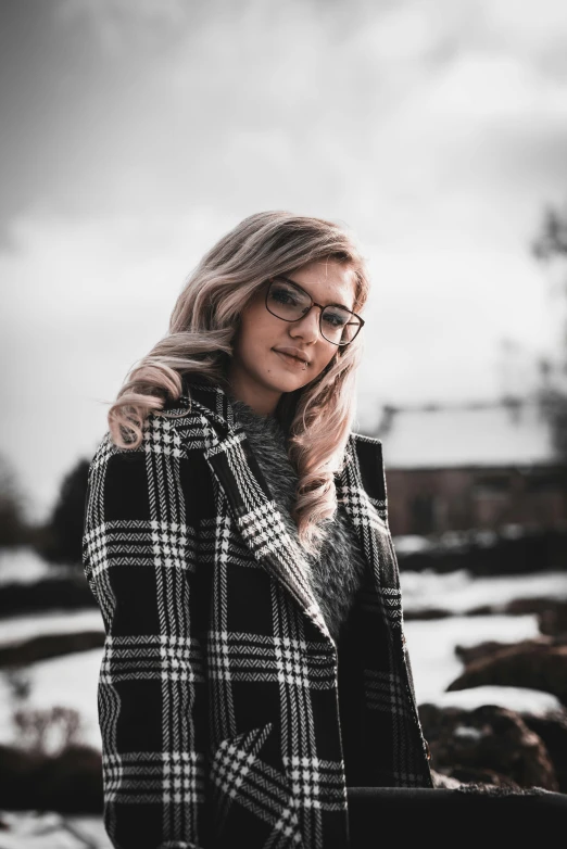 a woman wearing glasses standing in front of a snow covered field