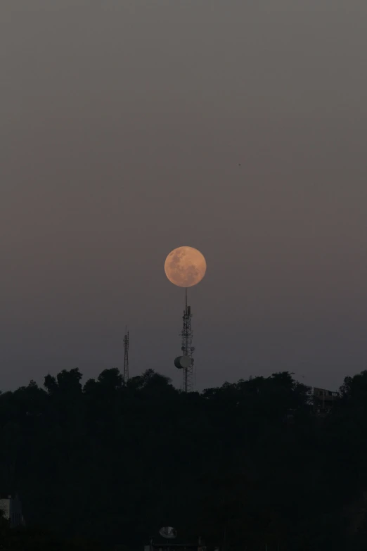 a large moon over a city with a tower and radio towers