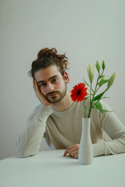 a man sits behind a vase with a red flower on the table