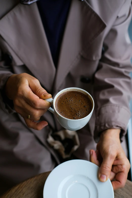 a person in brown jacket holding a cup with liquid