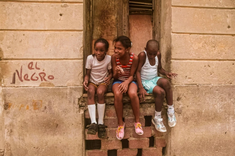 three children sit on steps near doorways with brick and concrete wall