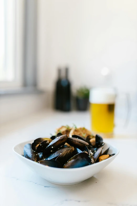 a bowl full of mussels with a beer behind it