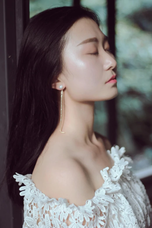 a woman with long black hair wearing an off shoulder top and earrings