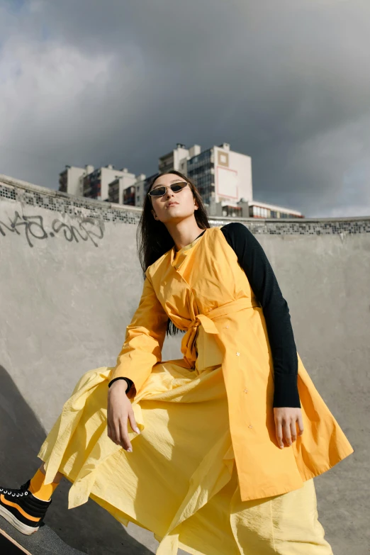 a girl wearing sunglasses and yellow dress on the edge of a skateboard