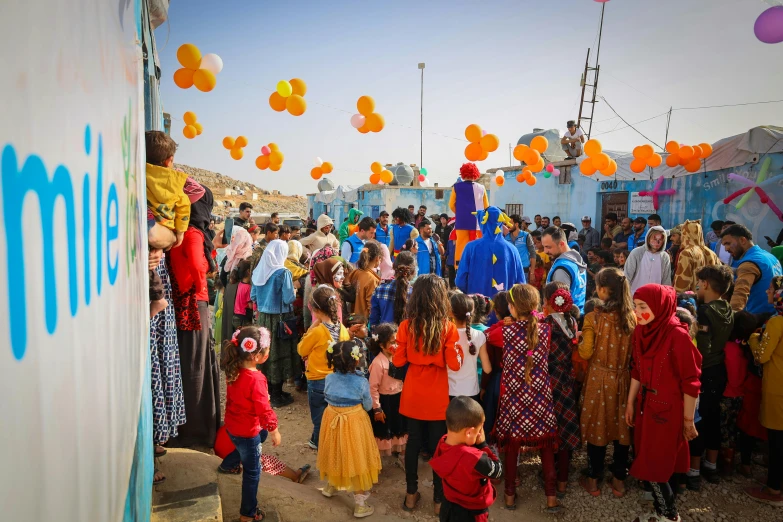 a crowd of children are standing around with balloons in the air