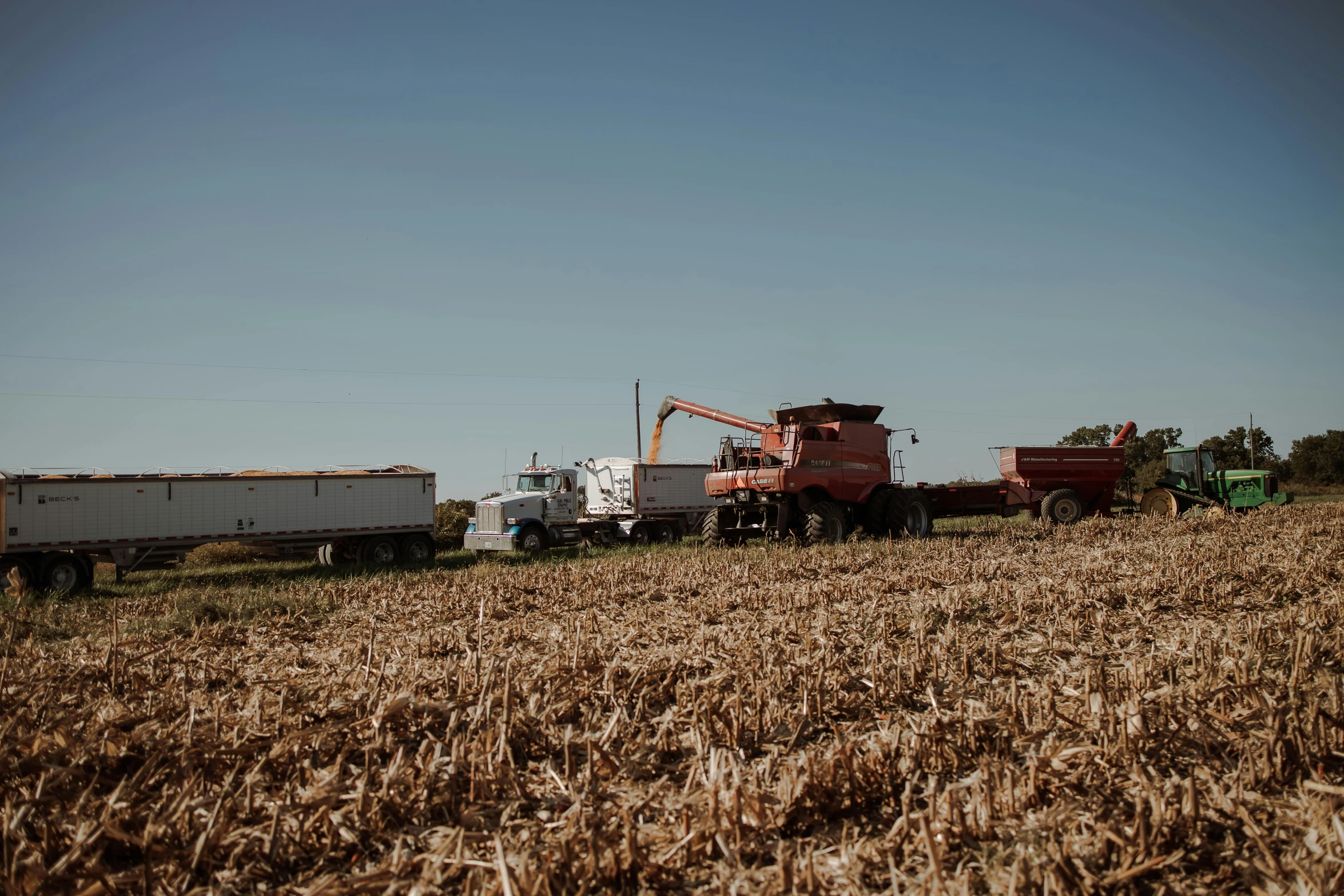 a large tractor and farm trailer are going through some field crops