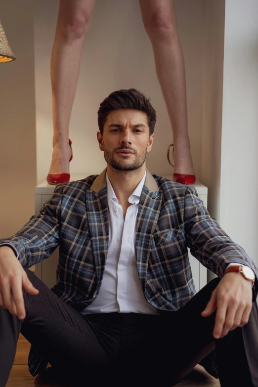 a man in a jacket and tie sitting on a stool