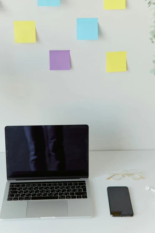a laptop, smart phone and sticky notes on a wall