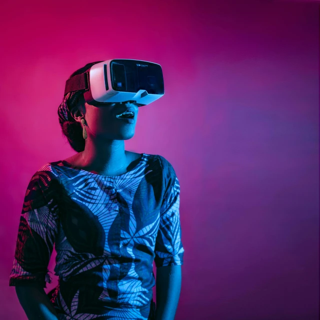 a woman standing in front of pink and blue background wearing a virtual - reality headset