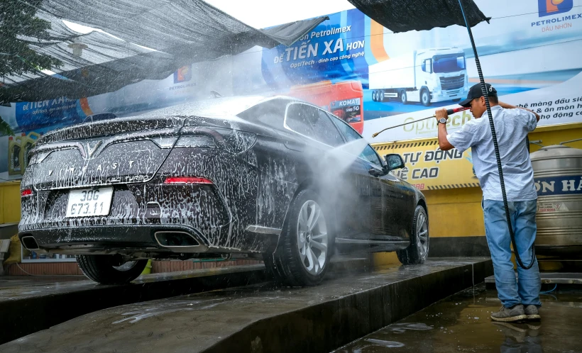 a man sprays water on a black car while it's being washed