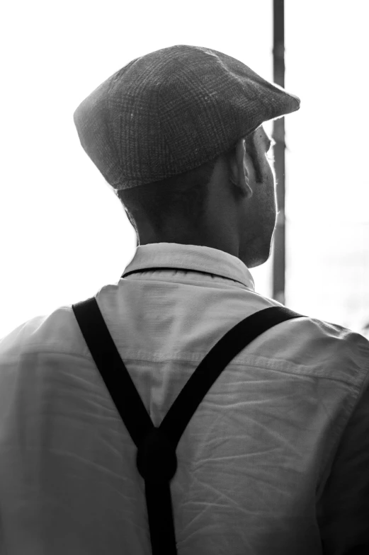 the back of a man's head wearing a hat and suspenders