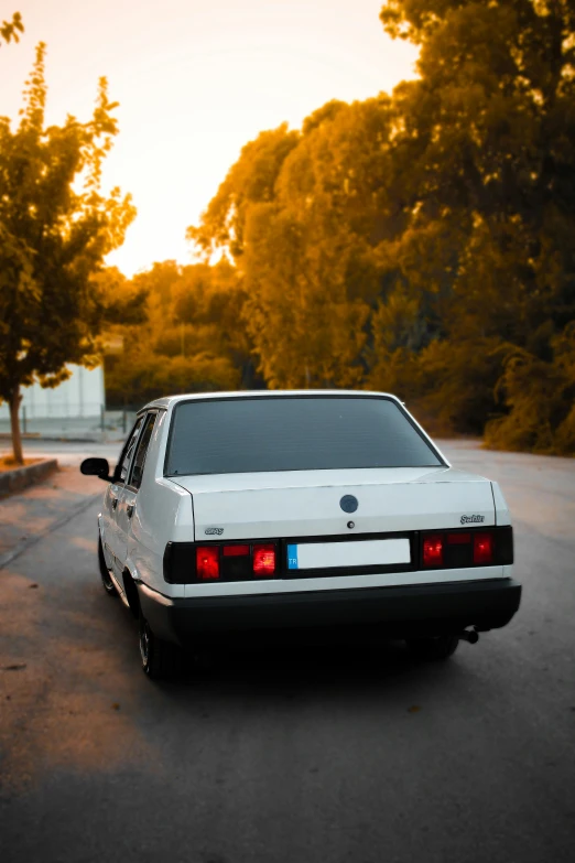 the back end of a white car sitting on the side of the road