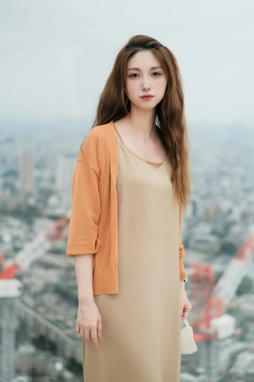 a woman stands in front of the cityscape, wearing a beige dress