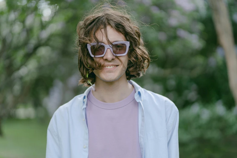 a man with sunglasses and a pink shirt standing next to trees