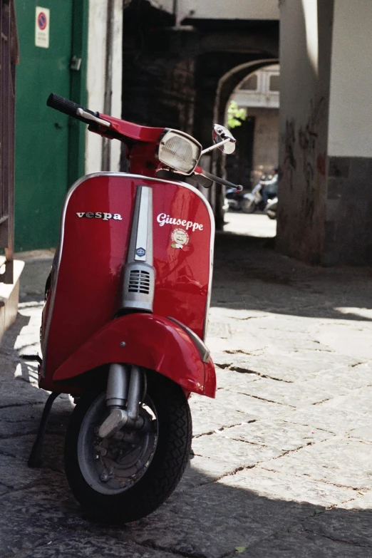 a red motor scooter is parked on a cobble stone street