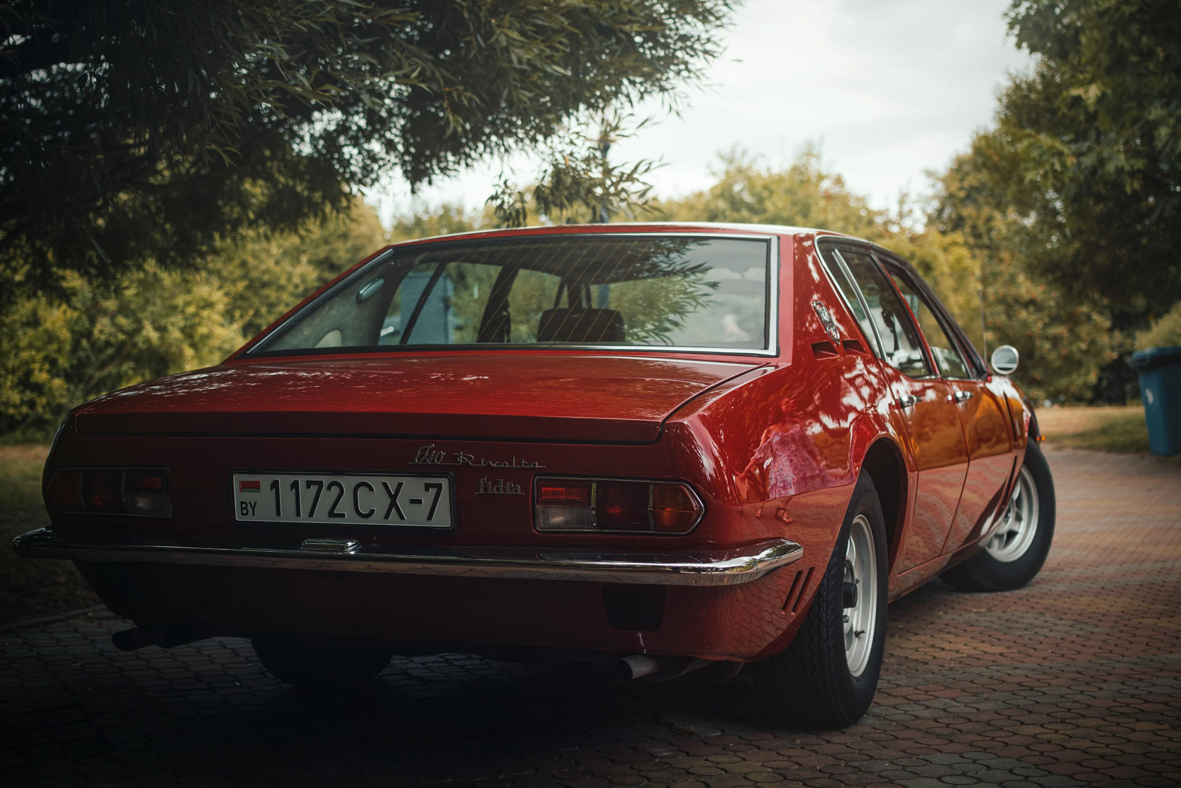 a classic car parked in a driveway surrounded by trees