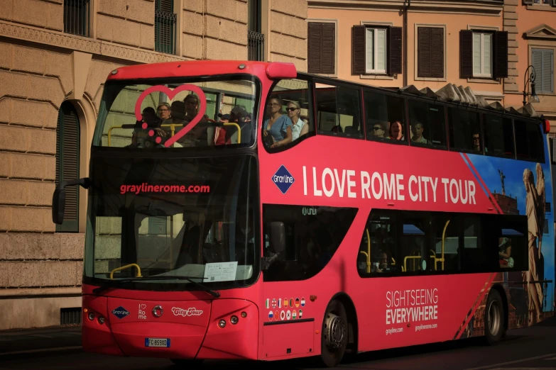 a pink tour bus drives down the street with passengers