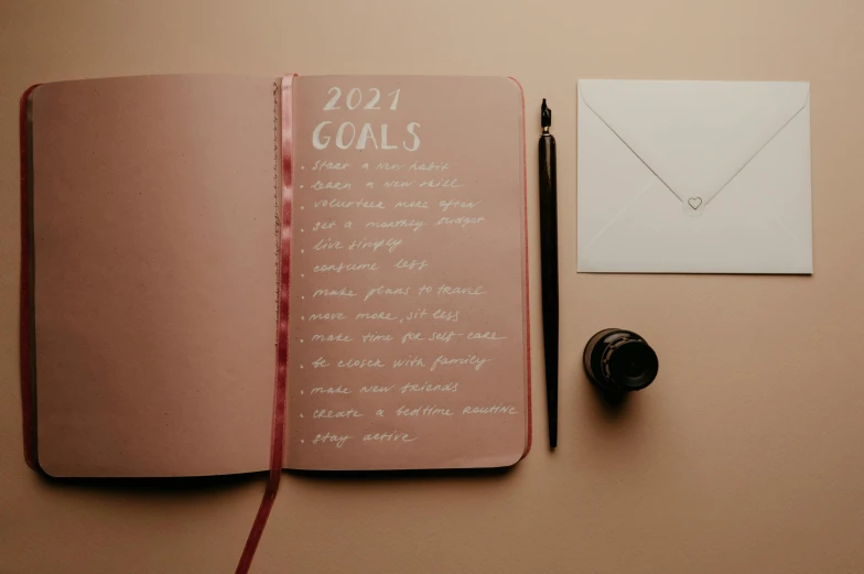 pink notebook with writing next to a pen and envelope