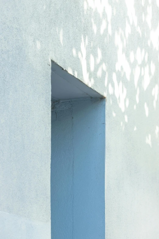 a white wall with a blue door and the shadow of trees on it