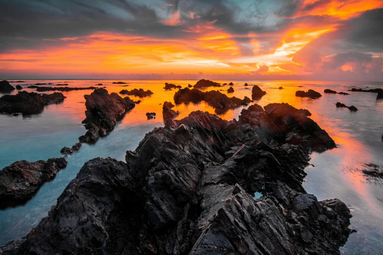 a picture of some water and rocks with the sun going down