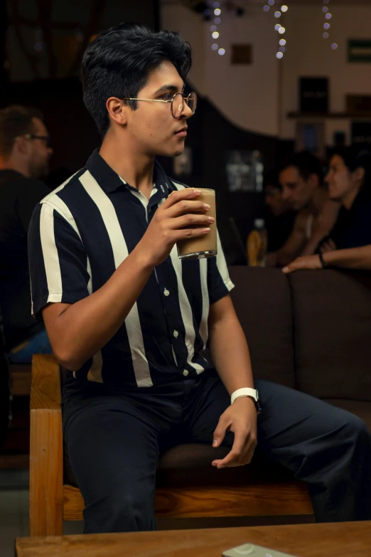 a man in a black and white shirt, glasses holding a drink