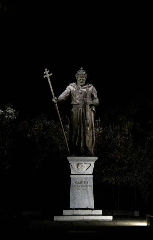 a statue stands tall in the night with a cross on its arm