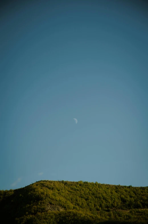 a moon is seen high in the sky over a hill