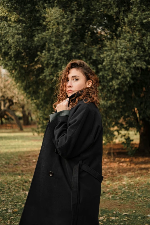 a woman stands in front of a tree with green leaves