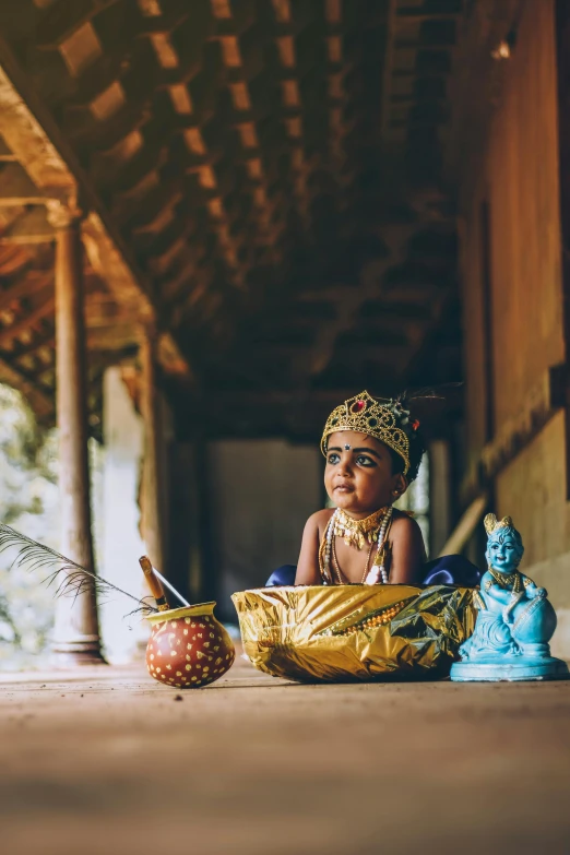 a young child wearing a gold headdress sitting on the ground with decorations