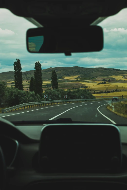 the view from inside a car on the road with mountains and fields