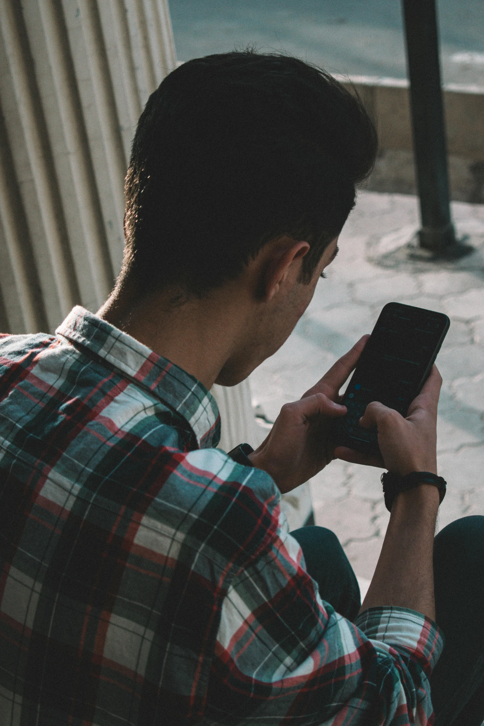 a man sitting next to the side walk holding a phone