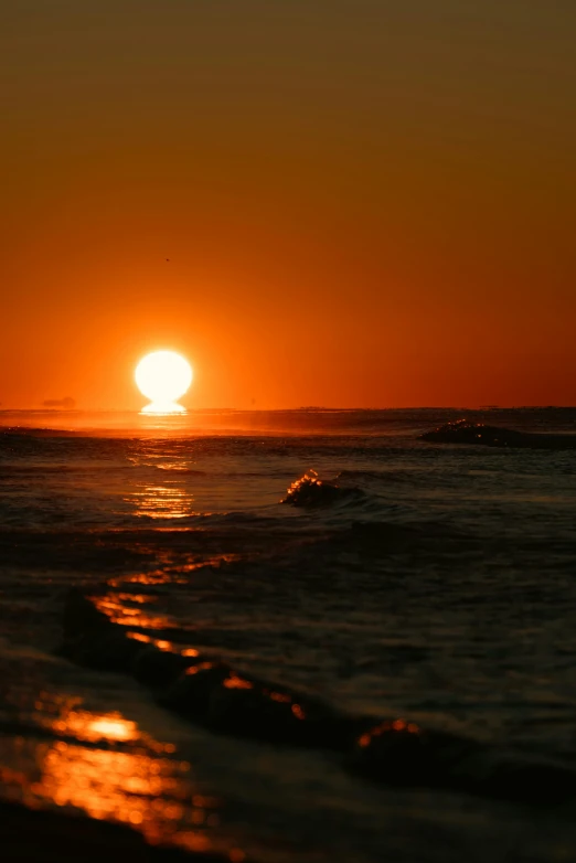 a sun rises over a sandy ocean during sunset